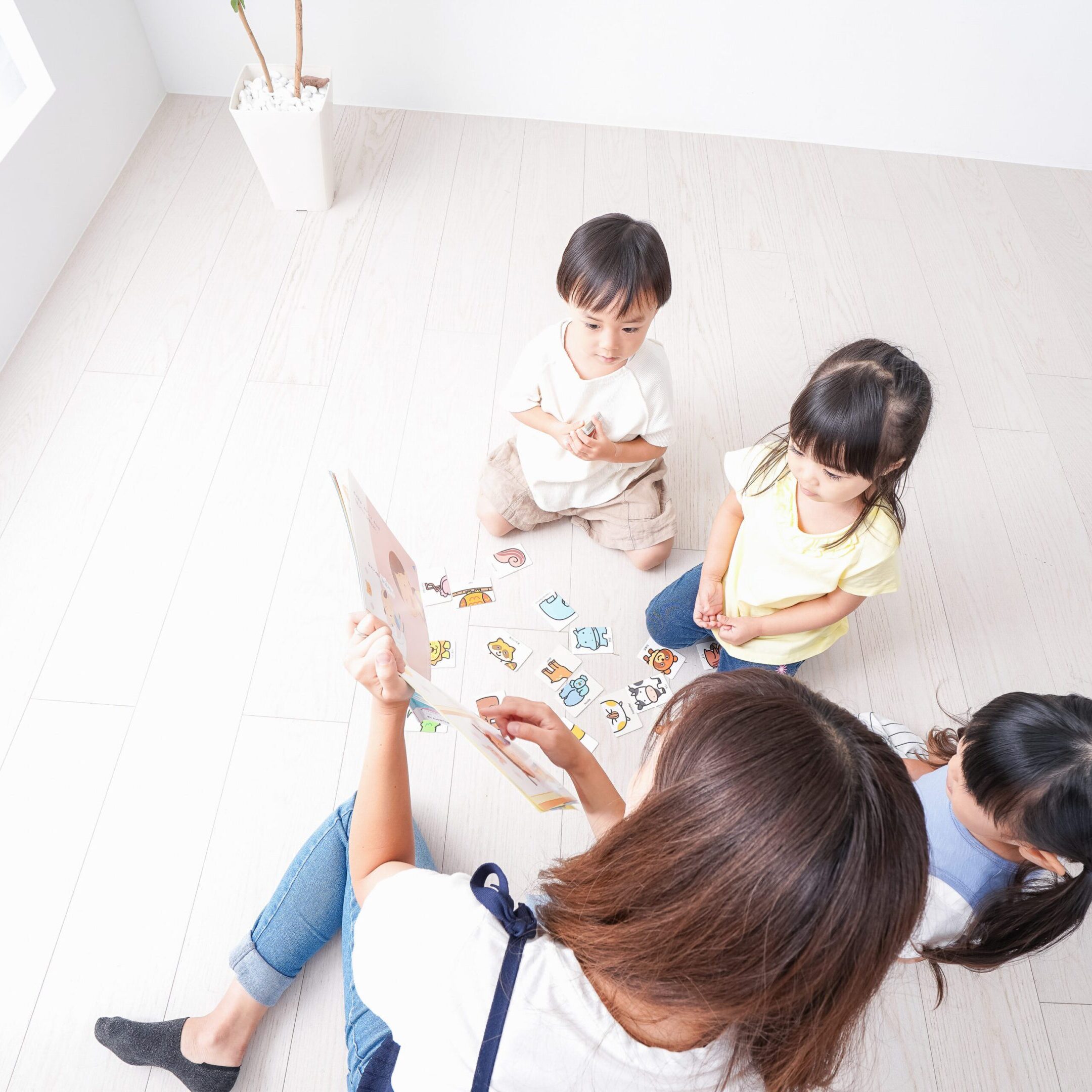 A caregiver plays with three children on the floor in a bright room.