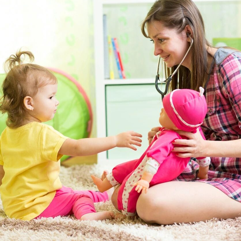 A young woman and toddler playing with a stuffed toy dinosaur.